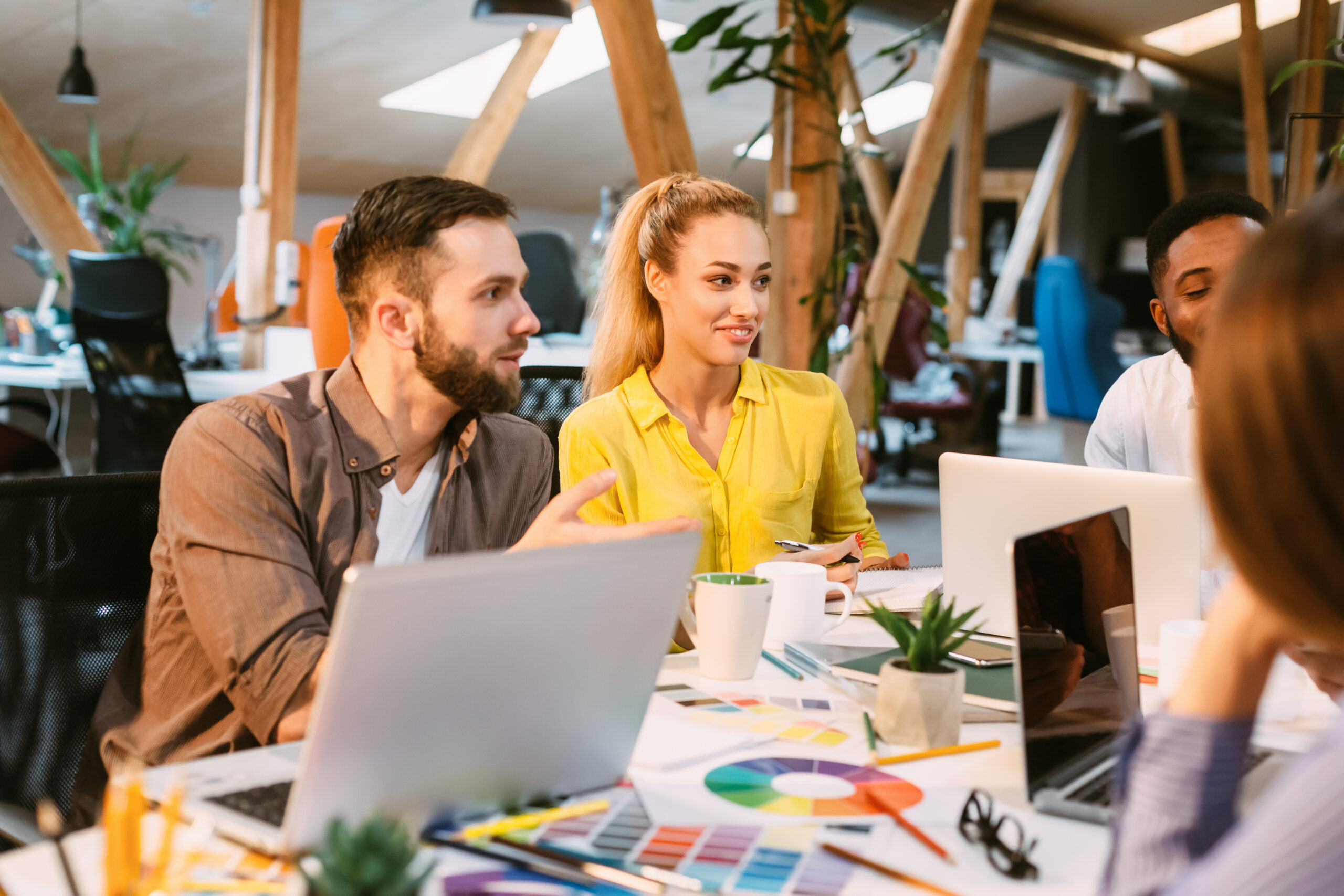 A diverse team of app developers collaborating around a desk with laptops and color palettes in a modern office.